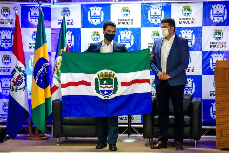 Prefeito JHC recebe de Rui Palmeira a bandeira de Maceió durante transmissão de cargo
